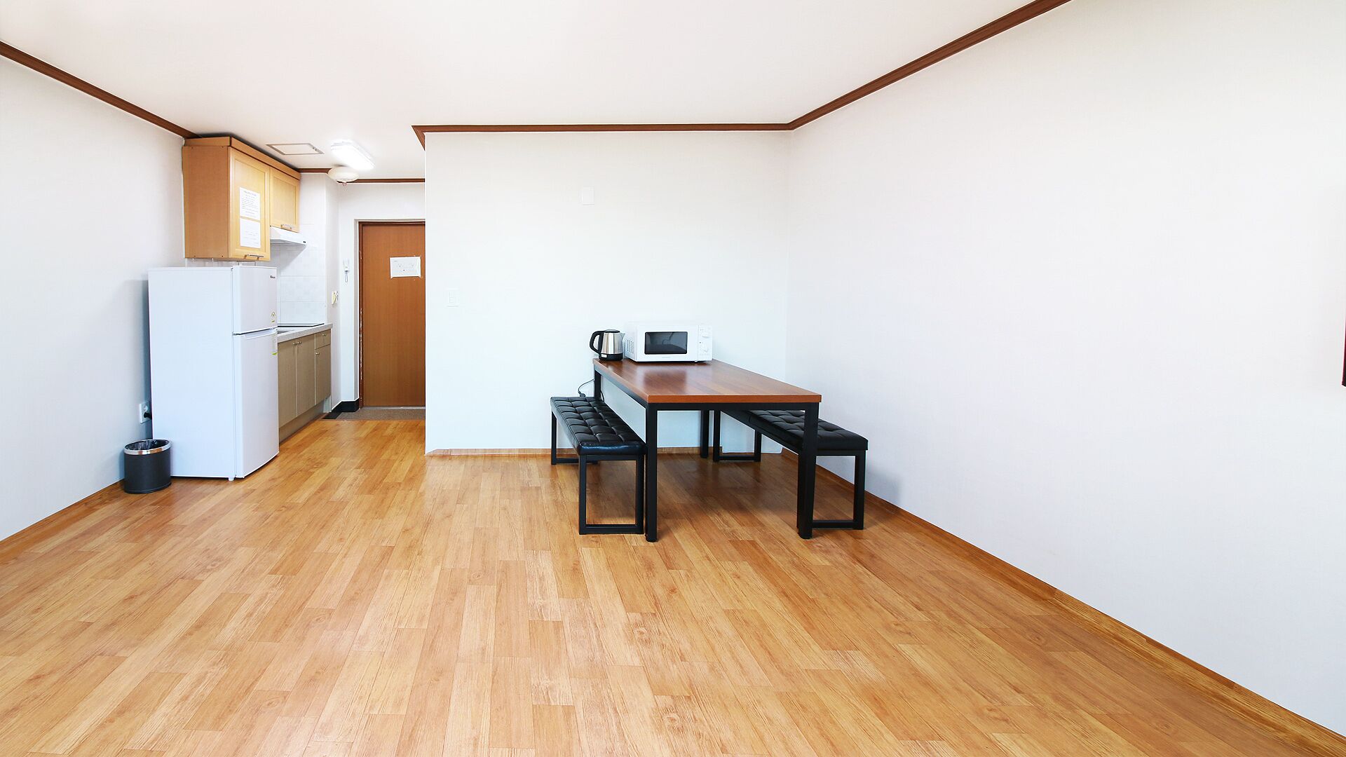 A compact kitchen with a refrigerator, microwave, and a wooden dining table with benches.
