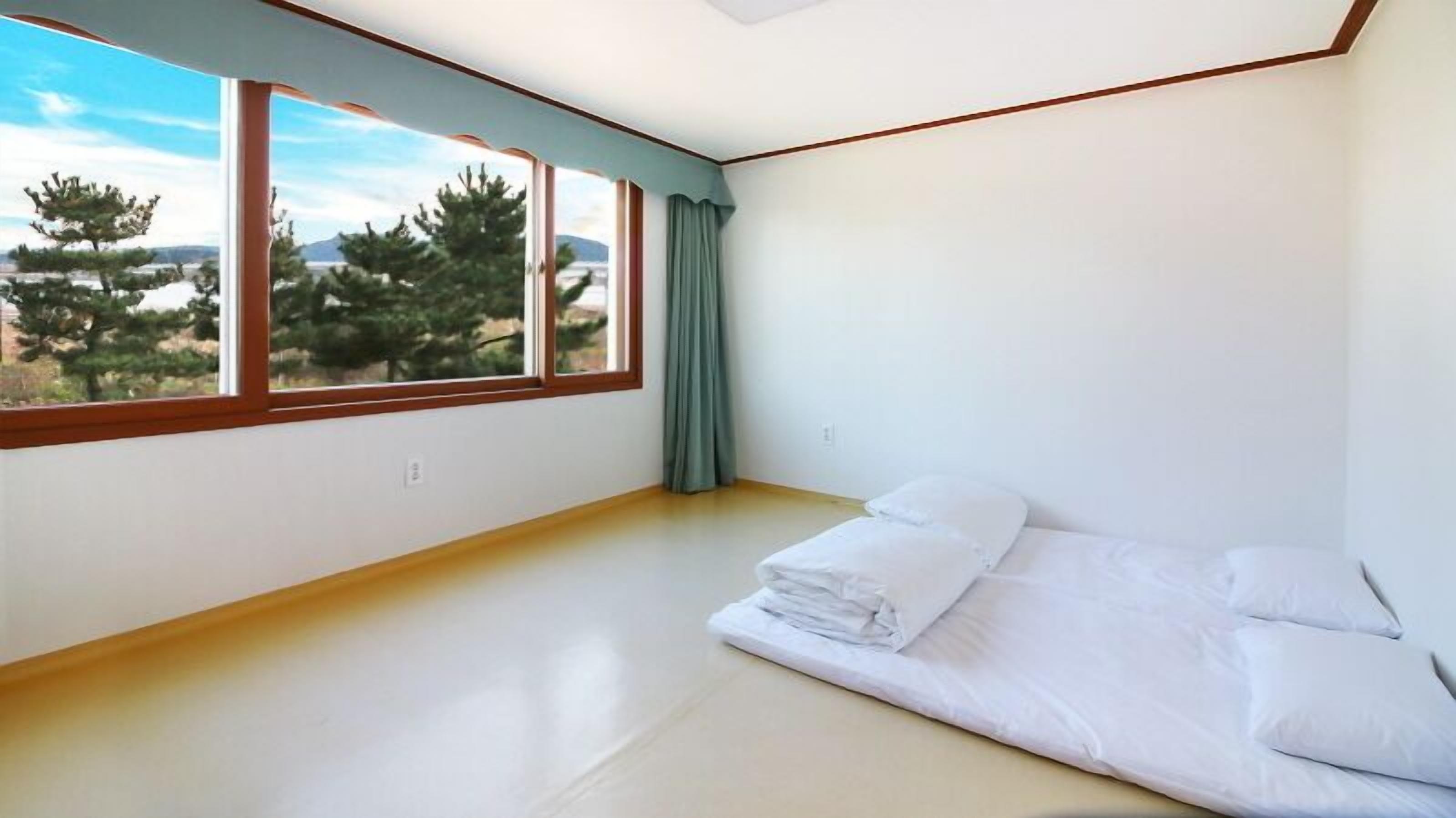 Een kamer met een groot raam, een bed met witte lakens en uitzicht op bomen en bergen.