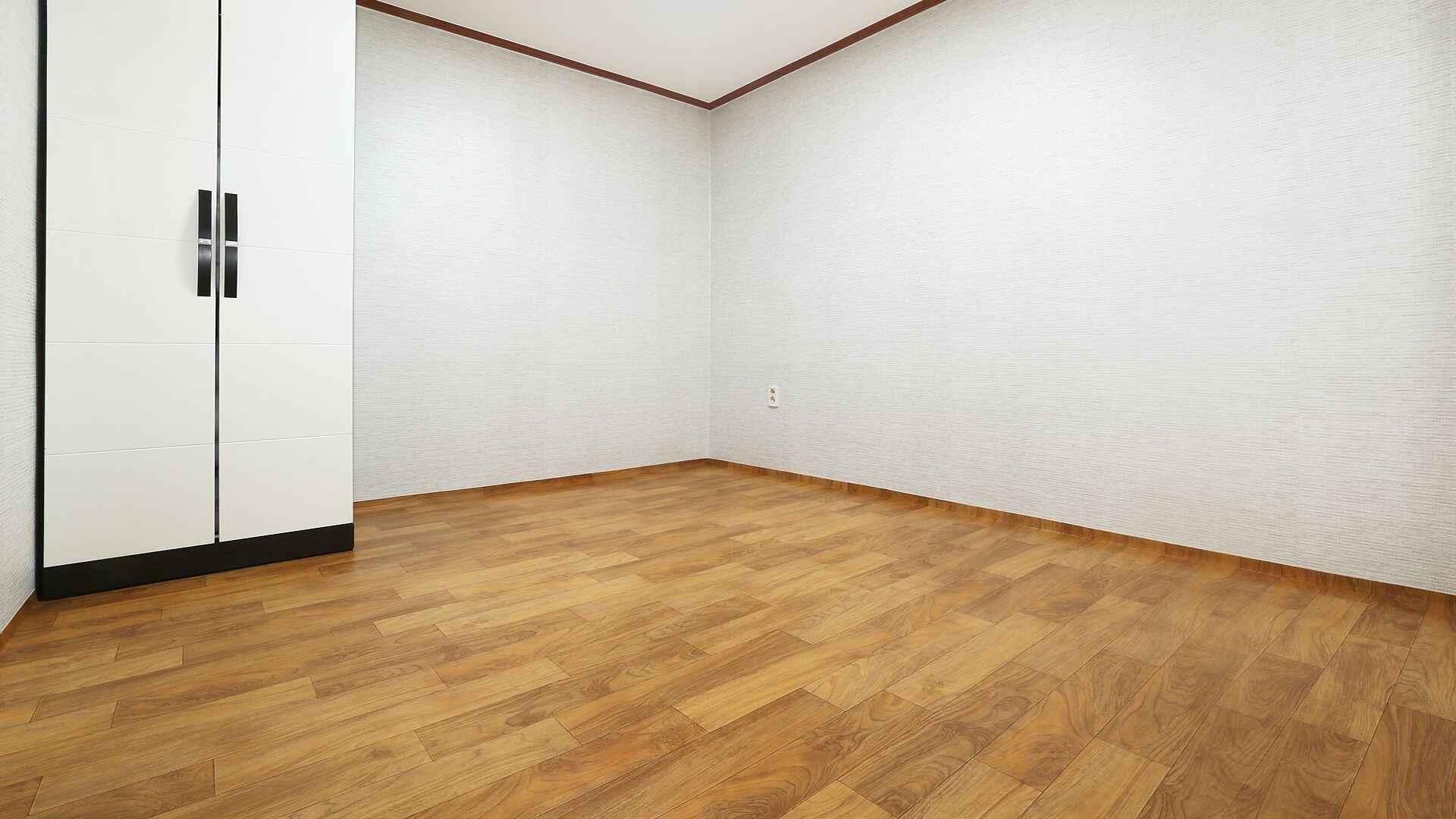 A room with wooden flooring, white walls, and a white wardrobe with black handles.