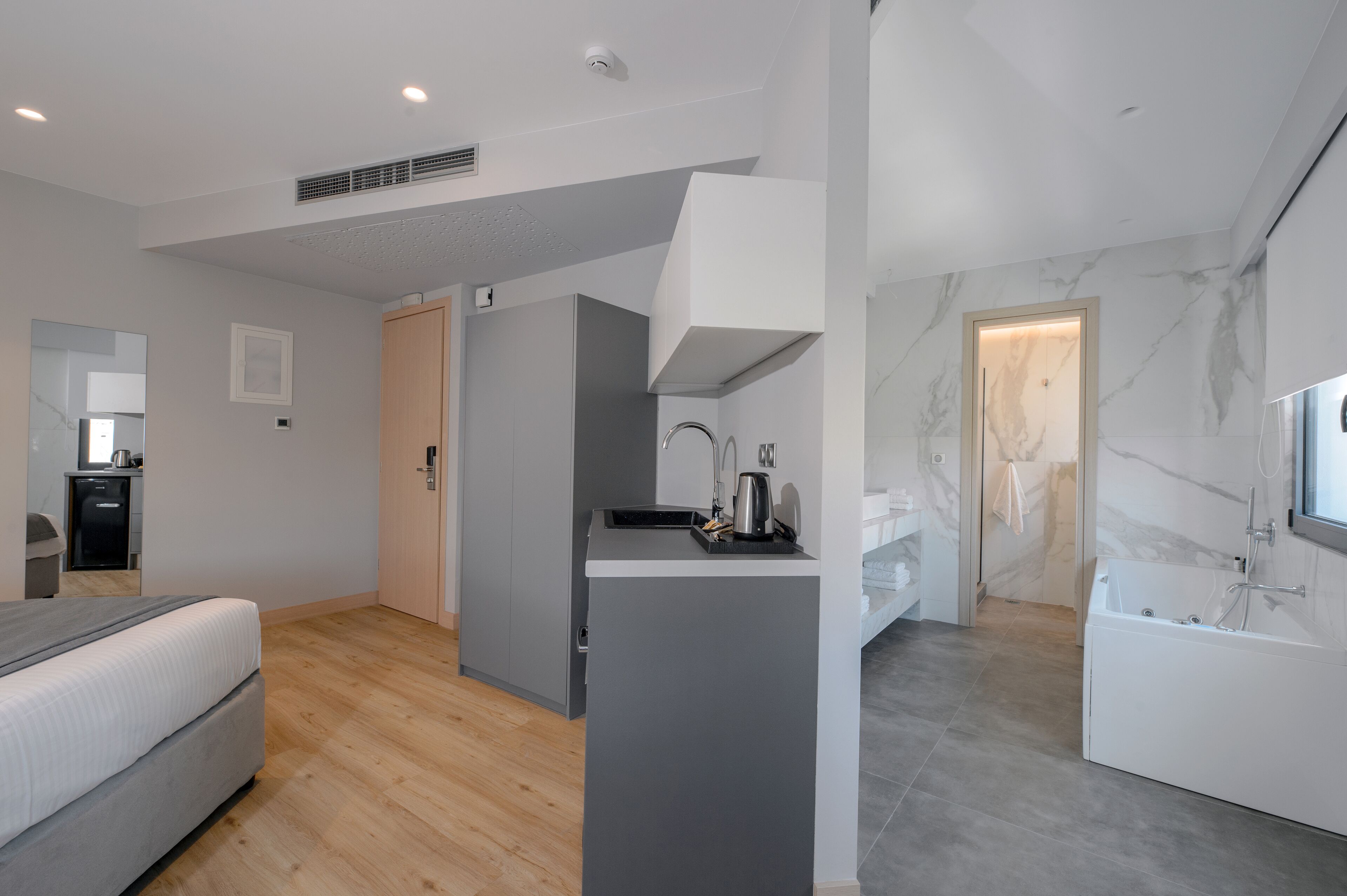 Habitación de hotel moderna con cama, kitchenette pequeña, baño con bañera y pared de mármol.
