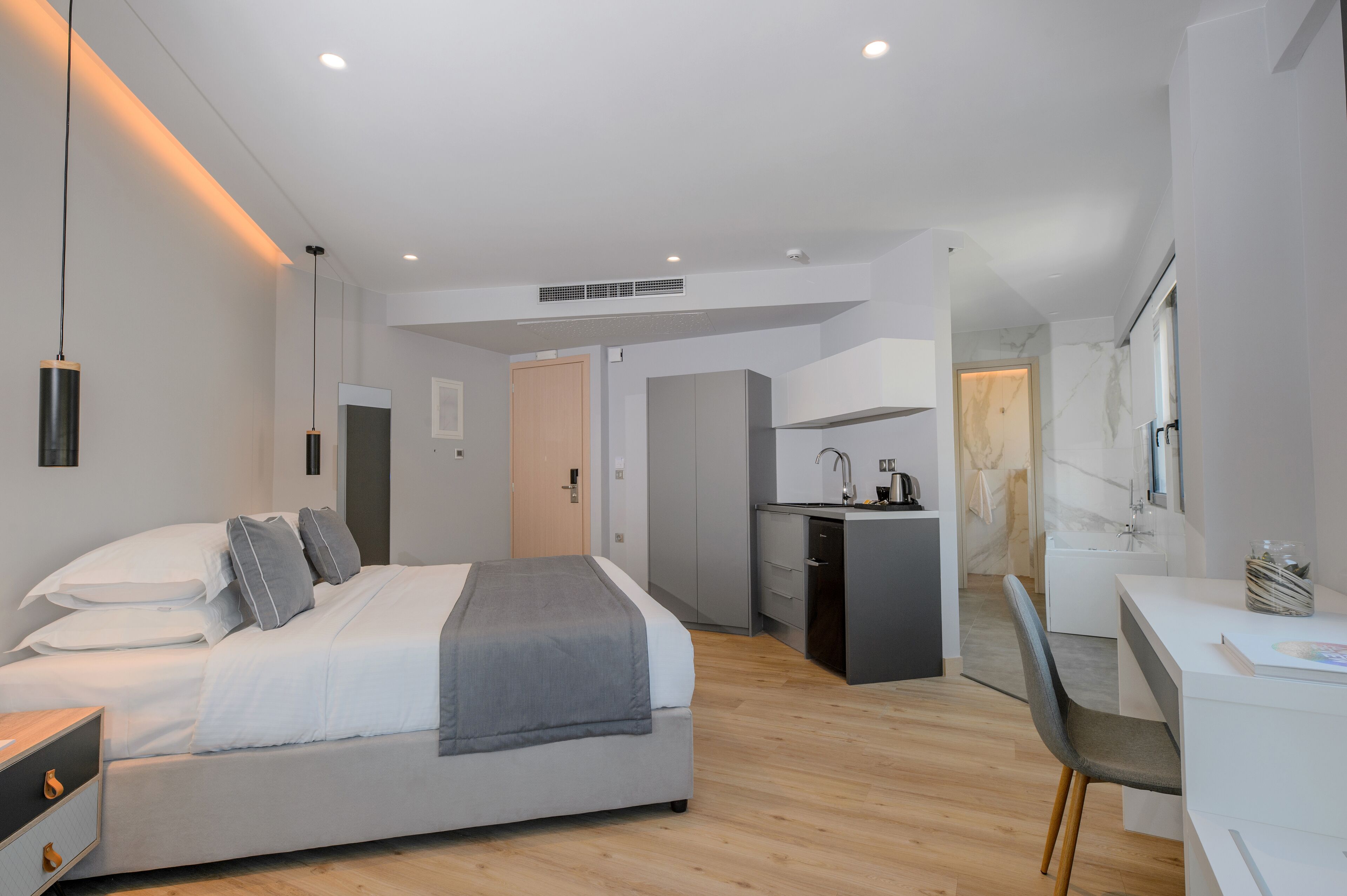 Een moderne slaapkamer met een bed, nachtkastjes, een bureau en een kitchenette.
