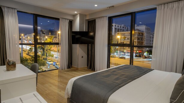A hotel room with a large bed, a desk with a chair, a TV mounted on the wall, and large windows with curtains. - The Convo Syngrou Apartments (Kallithea)