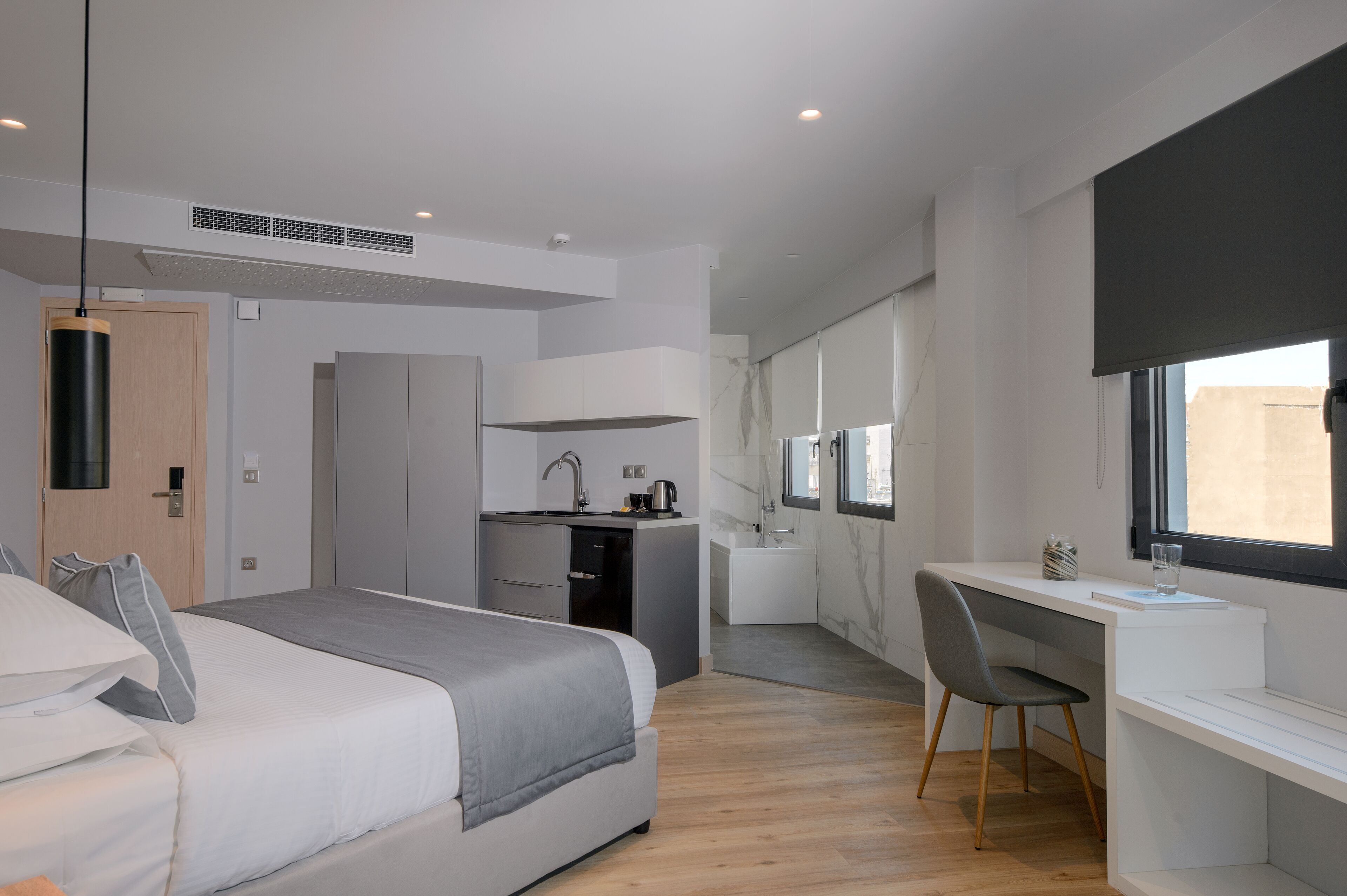 A modern bedroom with a bed, a desk, and a shower area.