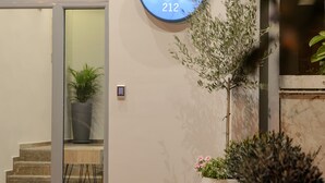 A modern building entrance with a glass door, a sign reading "The Convo 212", and a small garden area with plants and a potted tree. - The Convo Syngrou Apartments (Kallithea)
