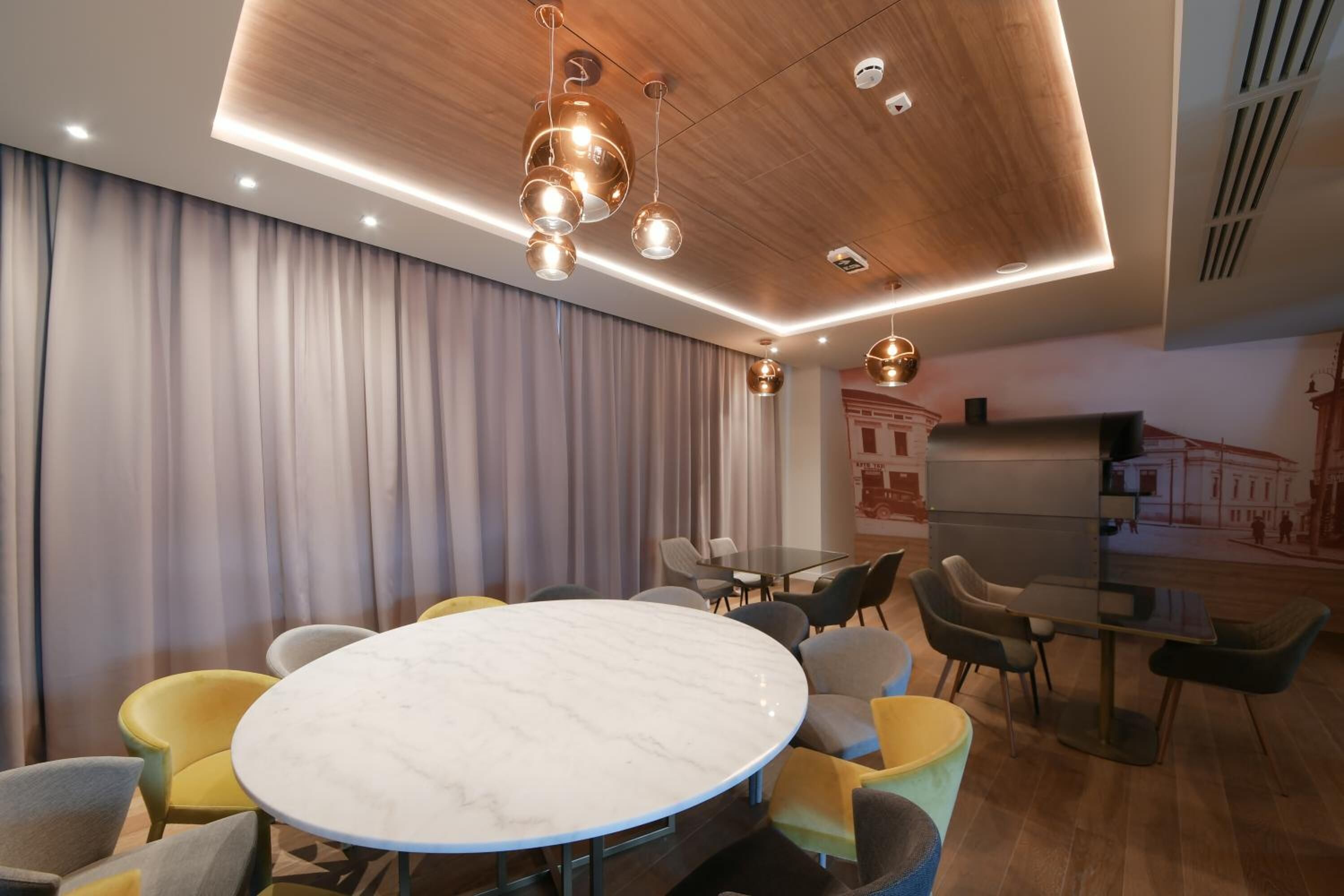 Una sala de conferencias moderna con una mesa redonda de mármol, sillas amarillas y grises, e iluminación colgante.