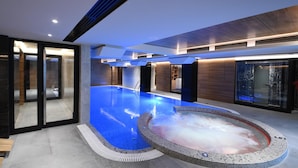 En modern inomhuspool med bubbelbad, omgiven av glasväggar och träpanel.