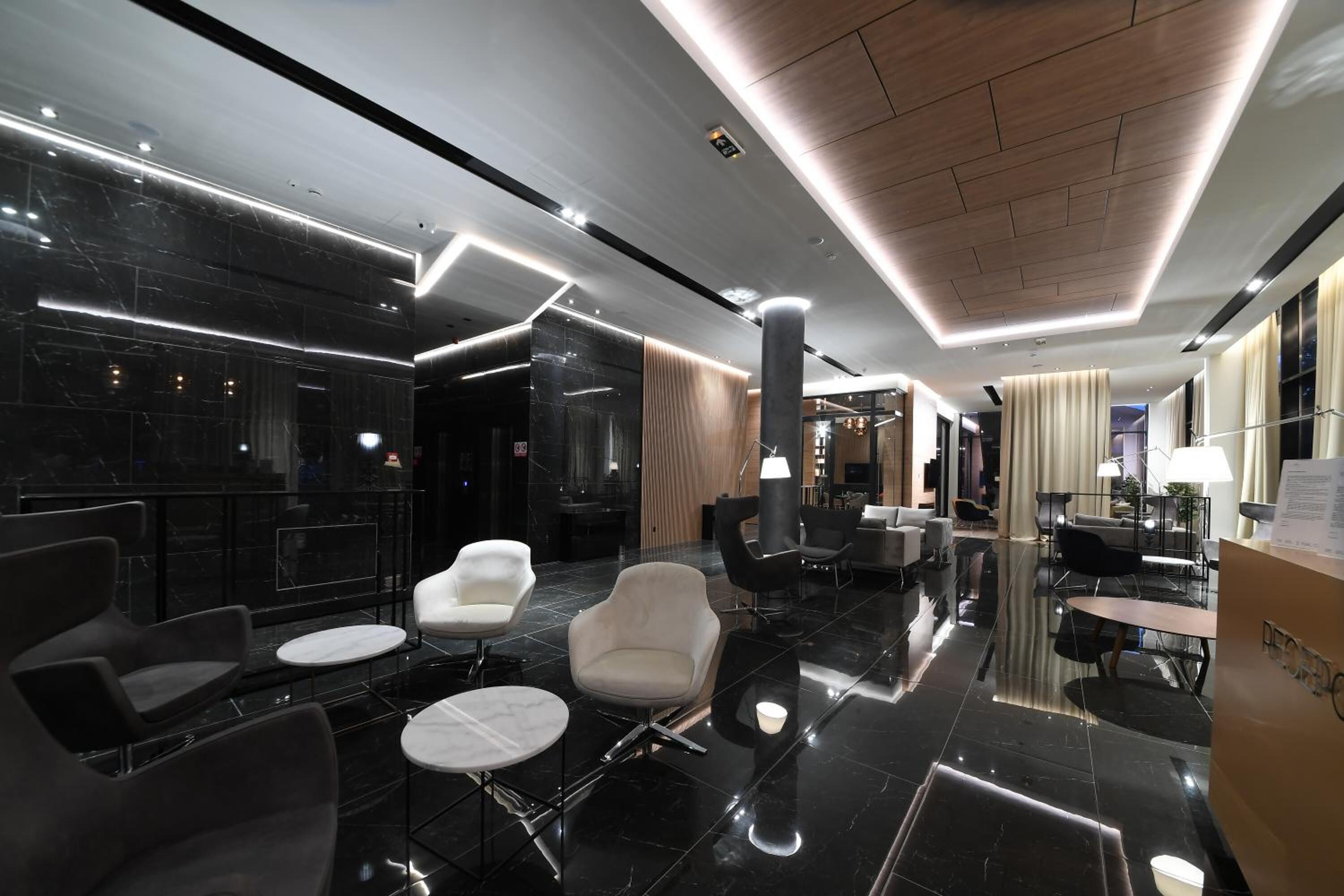 A modern lobby with black marble flooring, contemporary seating, and a wooden ceiling.