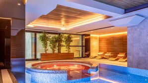 En modern inomhuspool med ett mosaikmönster, trädetaljer och sittområden.