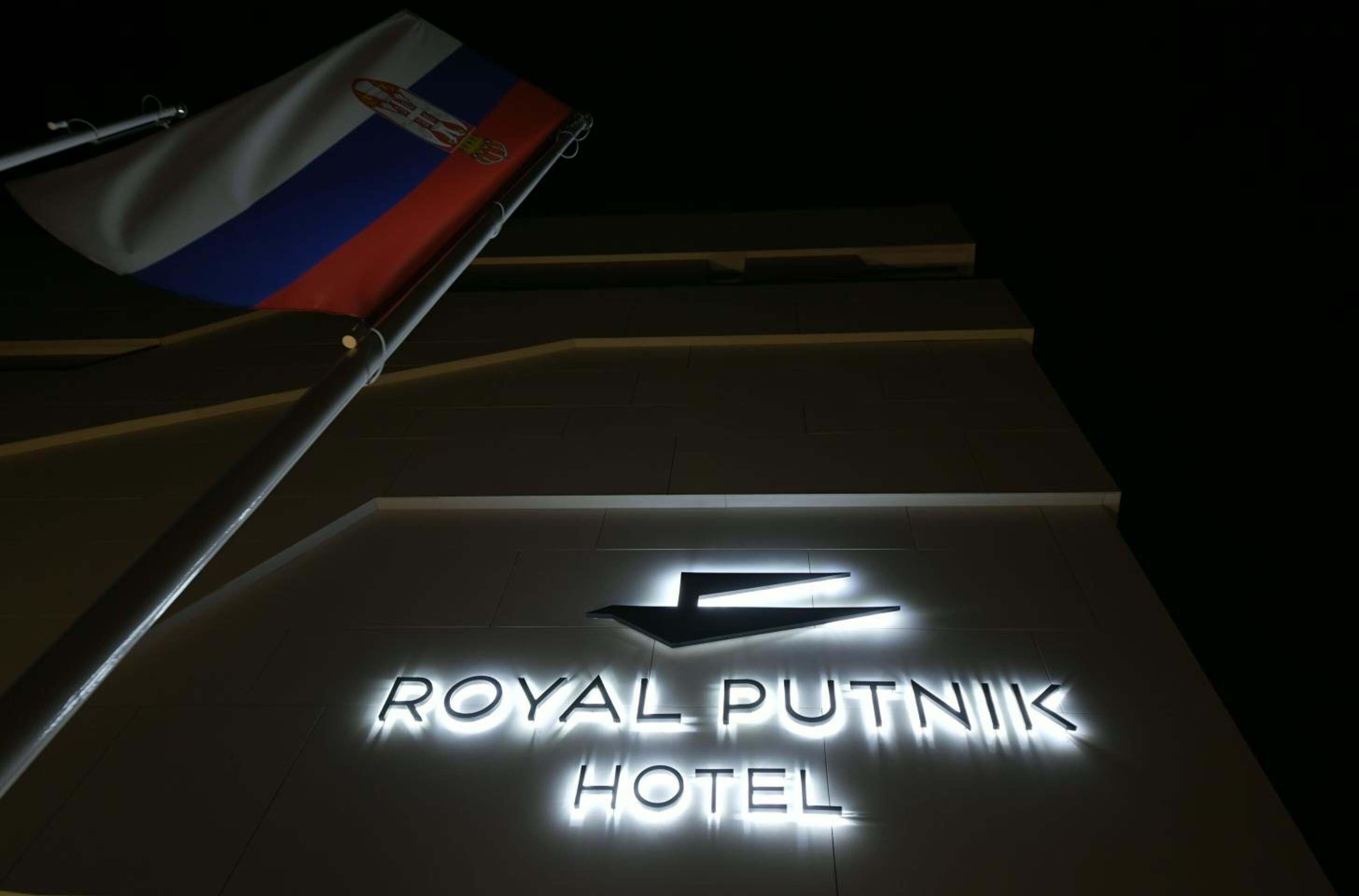 The entrance to the Royal Putnik Hotel with a flag and illuminated sign.
