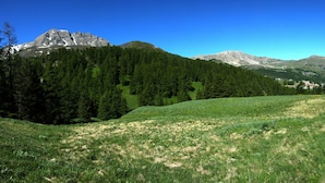 A mountainous landscape with a clear sky, a grassy field, and a trail leading towards a small settlement. - Mountain apartment rental (Vars)
