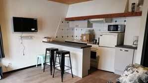 A compact kitchen with a microwave, stove, and small refrigerator. There are two stools and a small table. - Mountain apartment rental (Vars)