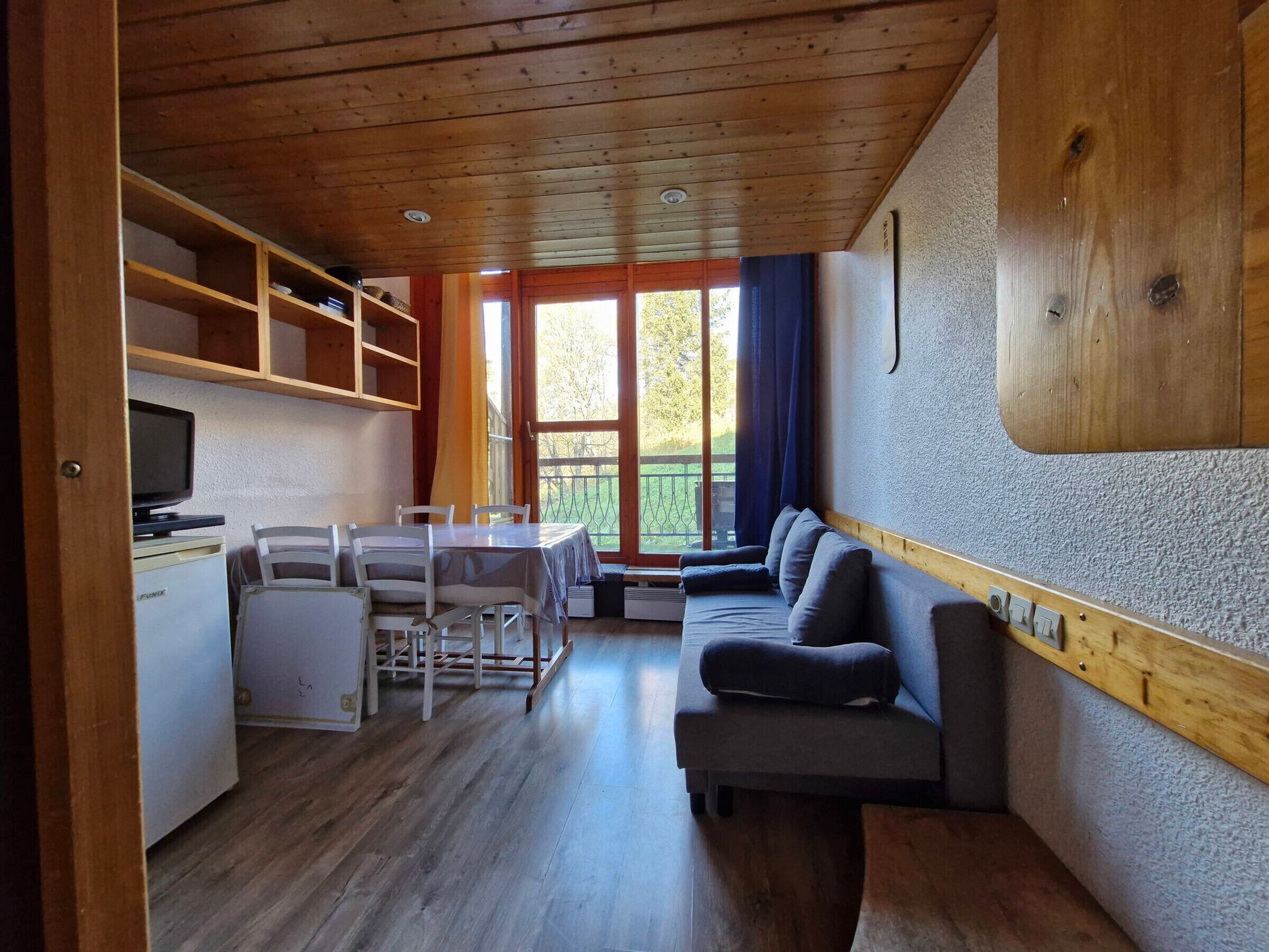 Una habitación acogedora con techo de madera, una mesa de comedor con sillas, un sofá y un televisor sobre un mueble.