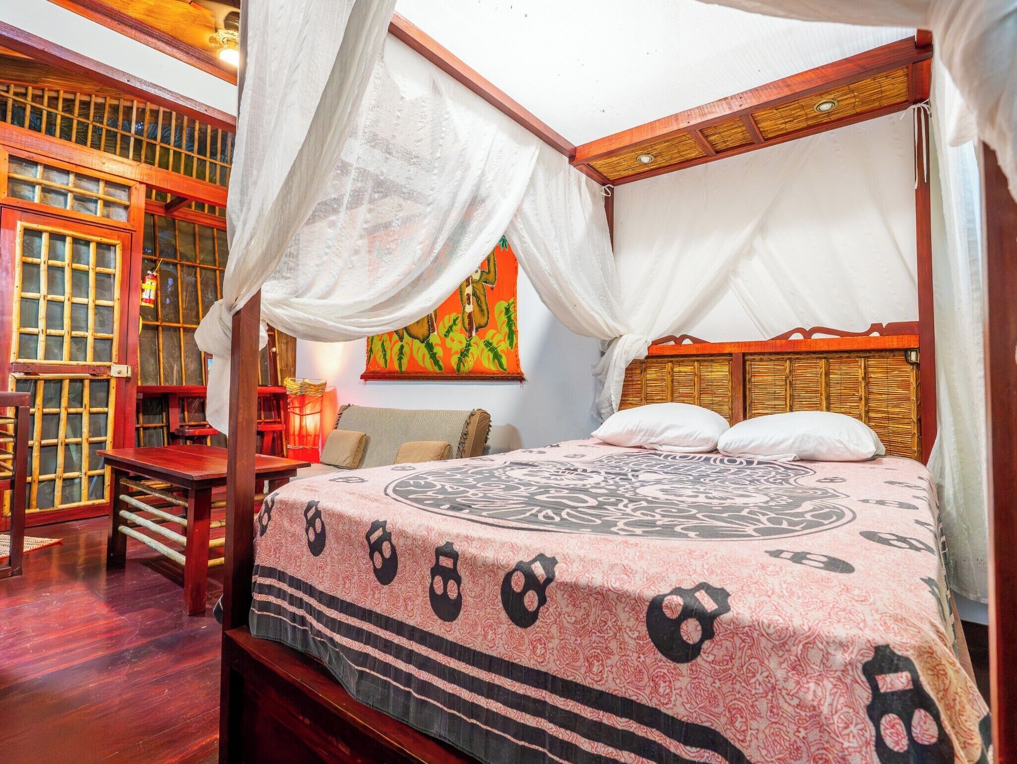 A traditional four-poster bed with a canopy, a wooden table, and a wall with a patterned tapestry.