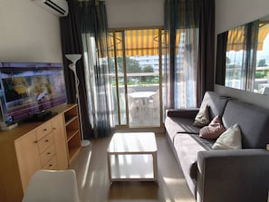 A living room with a flat-screen TV, a sofa, a coffee table, and a balcony with a table and chairs.