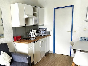 Una kitchenette compacta con microondas, cafetera y tostadora. Hay un pequeño comedor con una mesa y sillas.