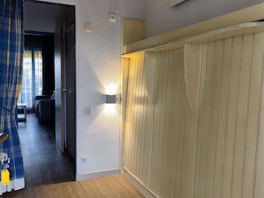 Una habitación con armario de madera, cama, escritorio y ventana con cortinas.