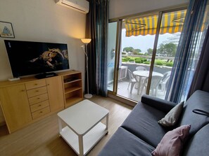 A modern living room with a flat-screen TV, a sofa, a coffee table, and a sliding glass door leading to an outdoor patio.