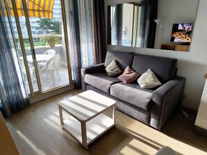 A living room with a grey sofa, a white coffee table, and a sliding glass door leading to an outdoor area.