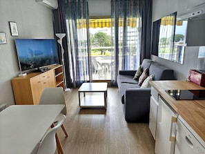 A compact living space with a sofa, a dining table, a TV, a kitchenette, and a view of the outdoors.
