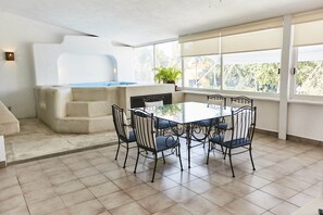 Una sala moderna con una mesa de comedor de vidrio, sillas de metal negro, un sofá color beige y un ventanal con vistas a zonas verdes.