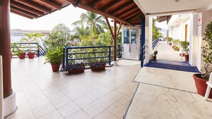 A covered outdoor area with potted plants, a blue railing, and a tiled floor leading to a building entrance. - Hotel Suites Ixtapa Plaza (Ixtapa)