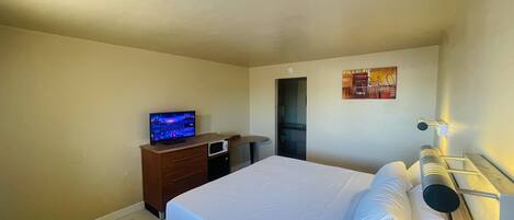 A hotel room with a bed, a television, a wooden dresser, and a microwave.