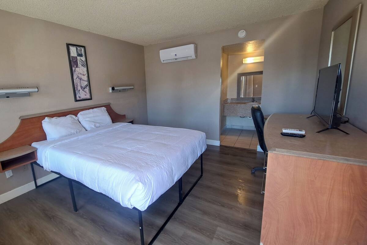 A hotel room with a bed, a desk, a TV, and a bathroom visible in the background.