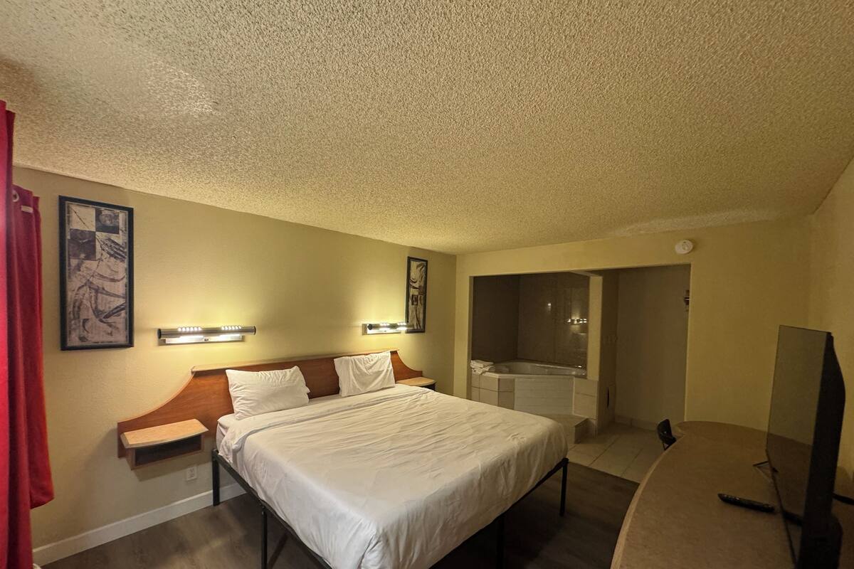 A hotel room with a bed, bedside tables, a TV, a bathroom with a bathtub, and a shower.