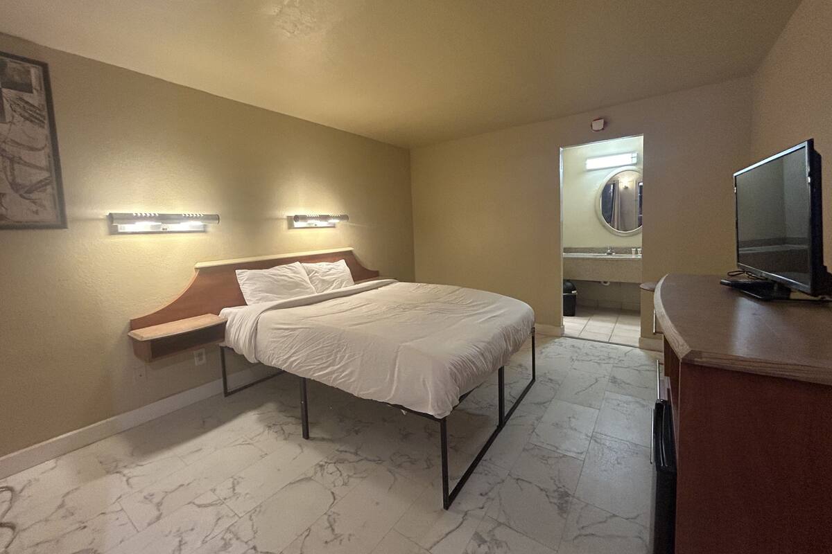 A hotel room with a bed, a desk, a television, and a bathroom with a mirror.