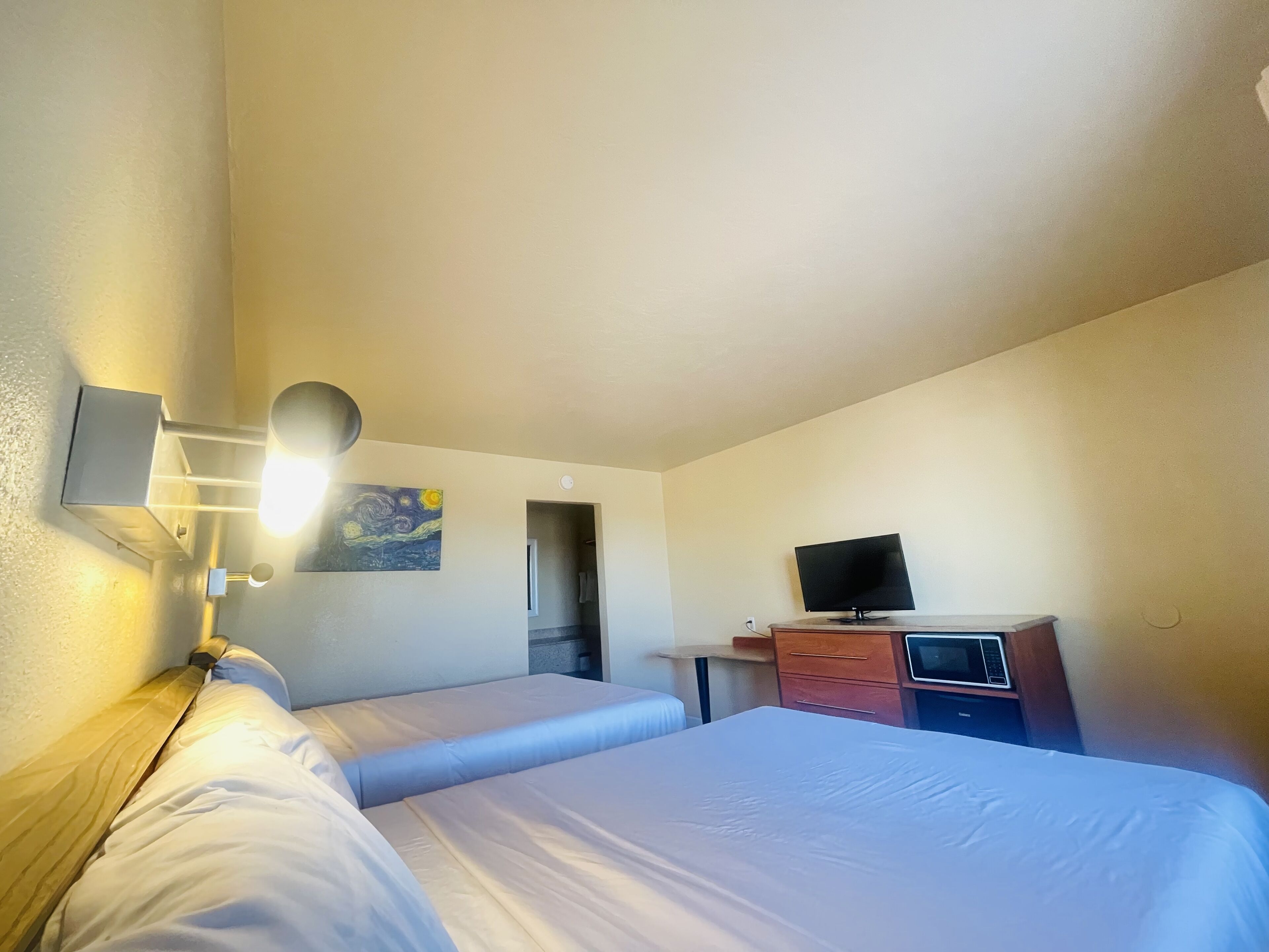 Ett hotellrum med två sängar, ett skrivbord med en tv och en väggmonterad lampa.