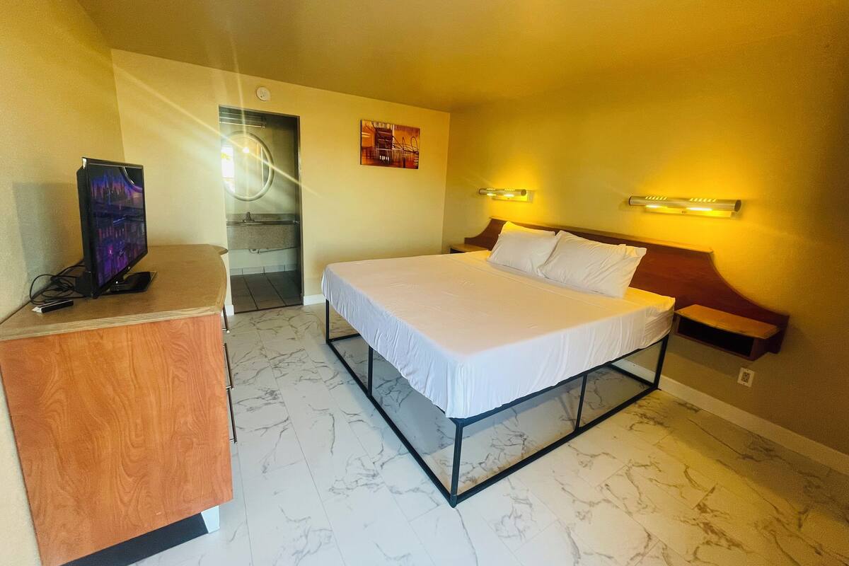 A hotel room with a bed, a desk, a TV, a bathroom, and a wall-mounted light fixture.