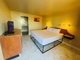 Habitación de hotel con cama, escritorio, televisor, baño y una lámpara fijada a la pared.