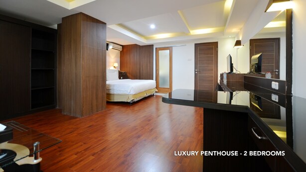 A luxury penthouse with two bedrooms, wooden flooring, a large bed, a vanity with a mirror, and built-in shelving. - Kasira Residence Serviced Apartment (South Tangerang)