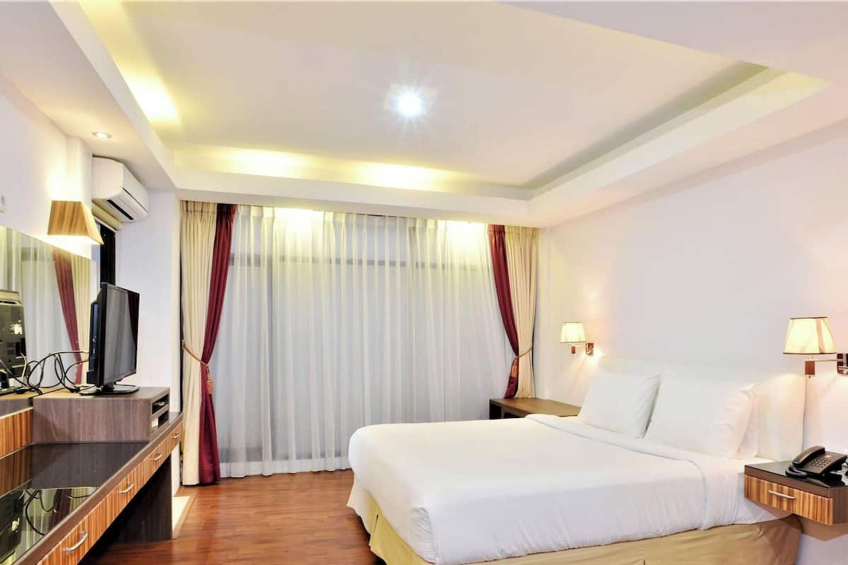 Una habitación de hotel con cama, lámparas de noche, un escritorio con computadora y ventana con cortinas.