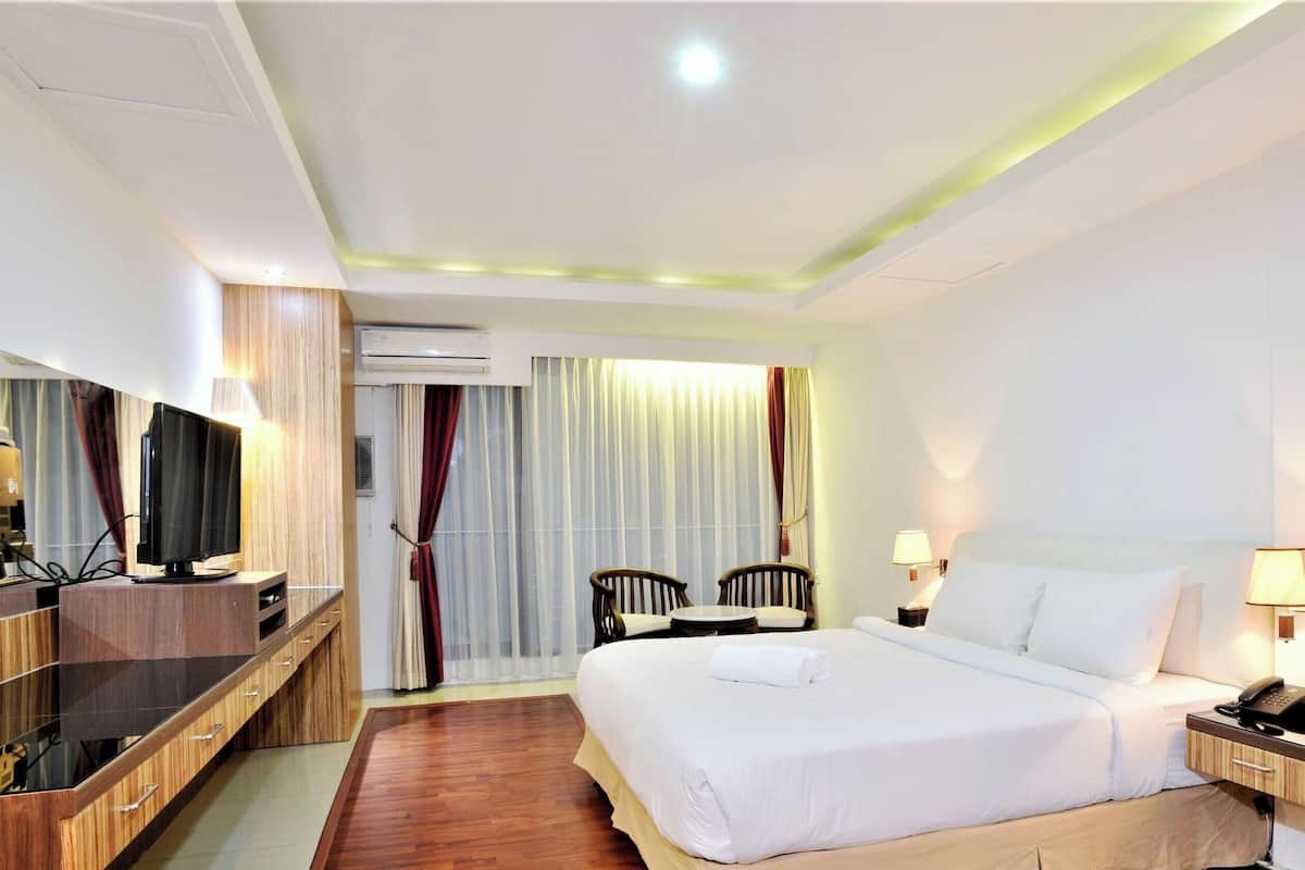 Una habitación de hotel con una cama, lámparas de noche, un escritorio con televisor de pantalla plana, una silla y un equipo de aire acondicionado.