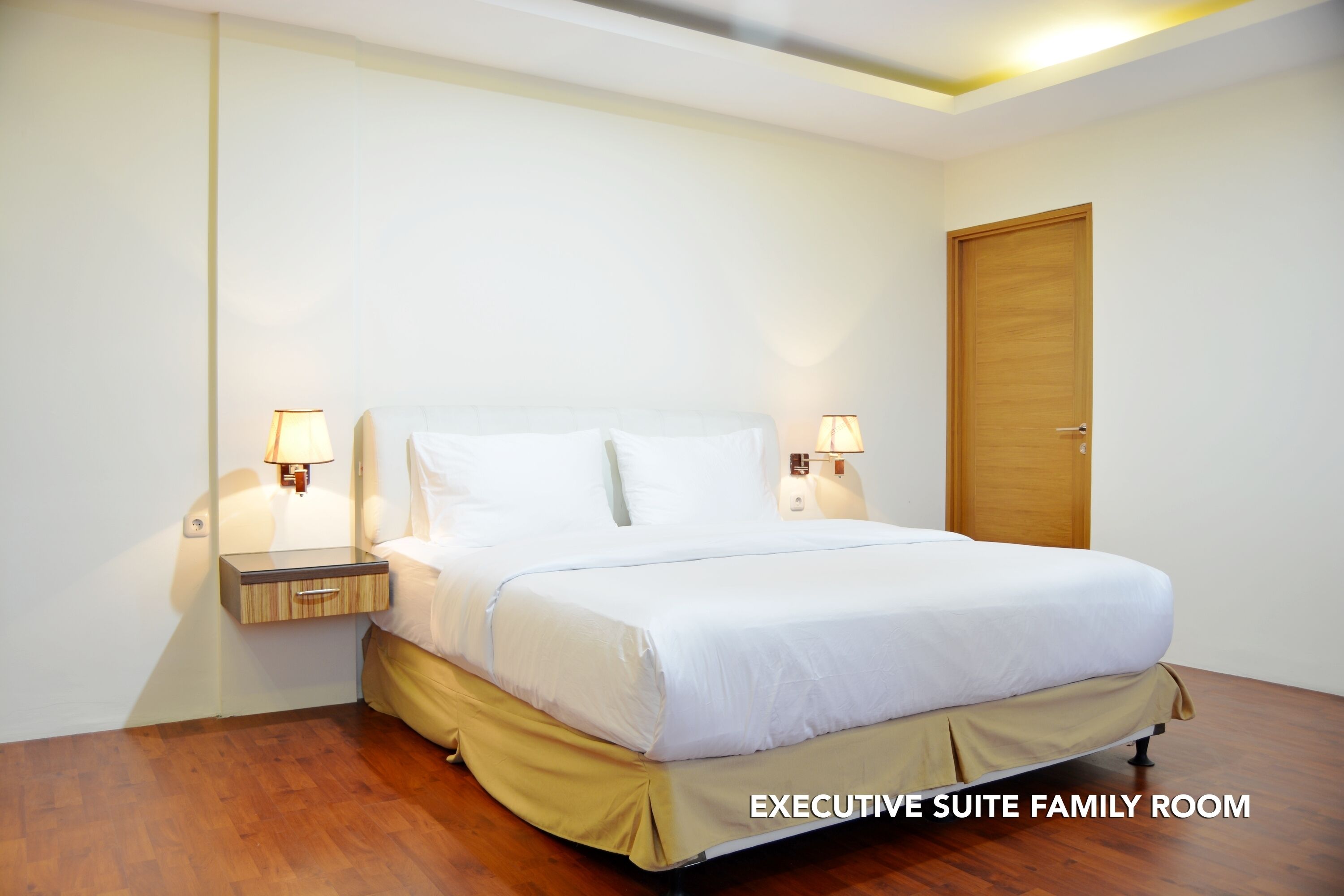 Une suite familiale de luxe comprenant un grand lit, deux tables de chevet avec lampes, une porte en bois et un plancher en bois.