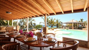 An outdoor dining area with a wooden table set for four, overlooking a swimming pool and palm trees. - The Carib House 5 Bedrooms And Pool Close To Beach (Falmouth Harbour)