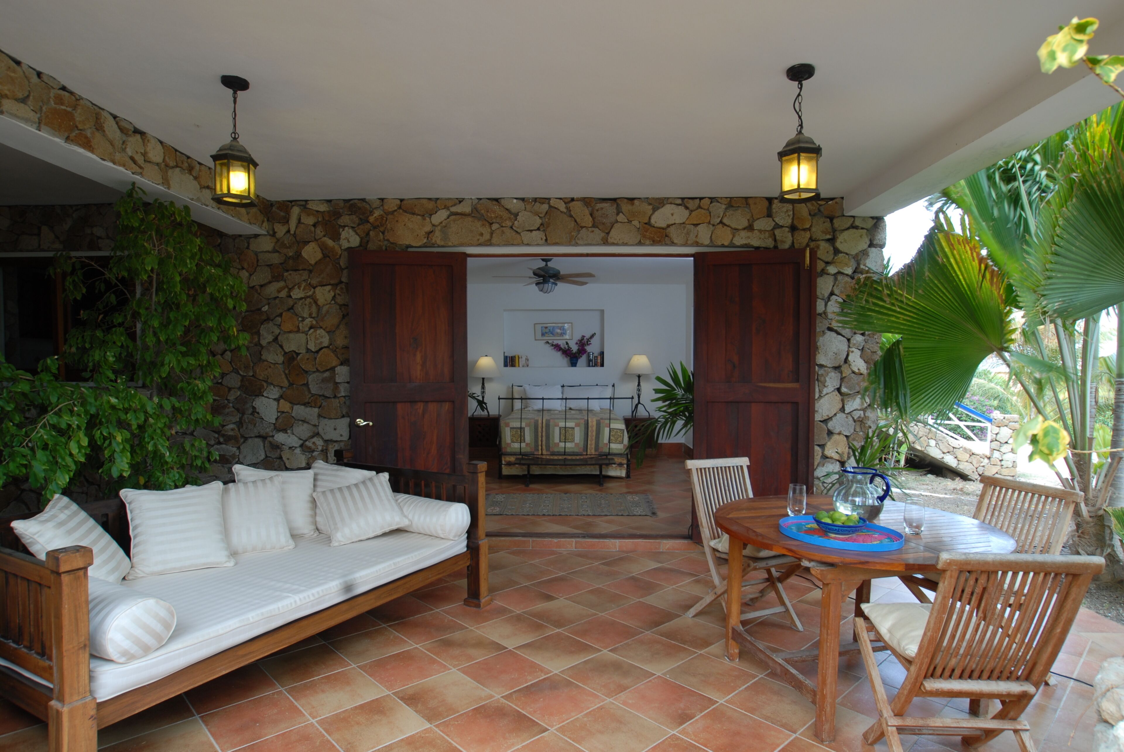 Un espace patio agrémenté d’un mur en pierre, d’un canapé en bois, d’une table à manger avec des chaises et de lanternes suspendues.