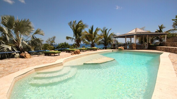 A clear swimming pool with a stone deck, lounge chairs, palm trees, and a gazebo. - The Carib House 5 Bedrooms And Pool Close To Beach (Falmouth Harbour)