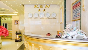 Zona de recepción de un hotel con una decoración en tonos dorado y blanco, que presenta un reloj grande con múltiples zonas horarias exhibidas sobre el mostrador.
