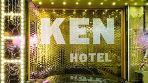 Entrada de un hotel con un gran letrero iluminado que dice "KEN HOTEL" y un coche estacionado al frente.