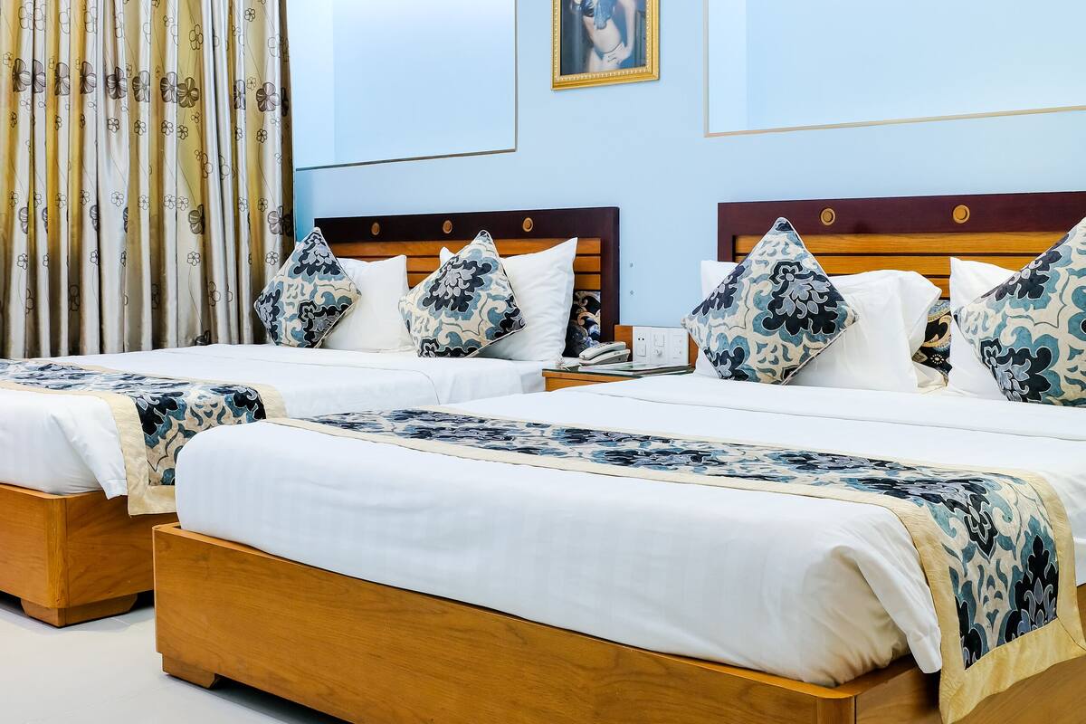 A hotel room with two wooden beds, a large round ceiling light, and a painting on the wall.