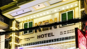 Un hotel con fachada bien iluminada, amplias ventanas y un coche estacionado frente a él.