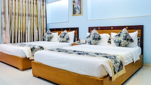 Habitación de hotel con dos camas de madera, ropa de cama blanca, mantas decorativas estampadas y un ventanal con cortinas.