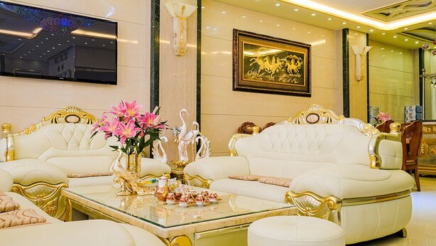 Una habitación lujosa con mobiliario blanco y dorado, que incluye un conjunto de sofá y una mesa de centro de cristal con objetos decorativos.