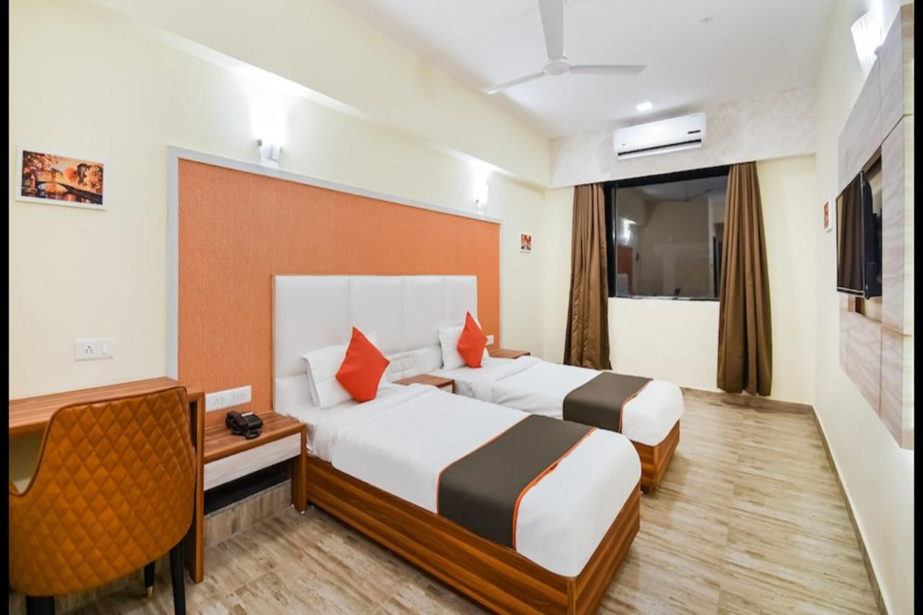 A hotel room with two beds, a desk, a chair, and a TV.