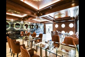 A modern restaurant with glass tables and brown leather chairs, featuring a unique wall with circular cutouts and a wooden ceiling. - Hotel Golden I (Raipur)