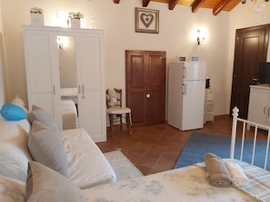 Um quarto com cama, guarda-roupa, uma cadeira de madeira pequena, frigorífico branco e televisão.