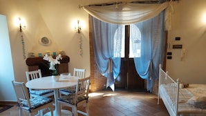 A dining area with a round table, chairs, and a chandelier. There is a bed with a striped blanket and a white headboard.