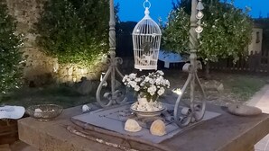 A stone table with a white birdcage and flowers, surrounded by greenery and a stone wall.